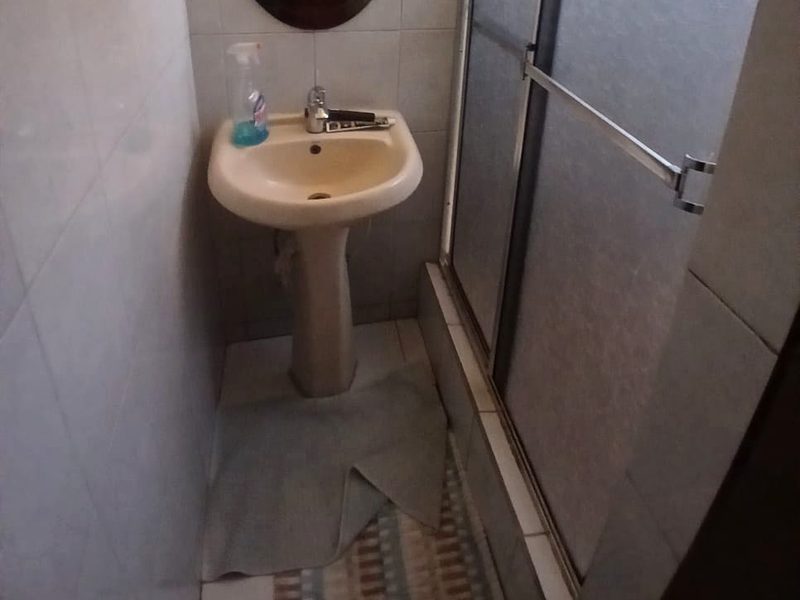 A tiled bathroom with a pedestal sink and a glass-panelled shower enclosure with a towel bar
