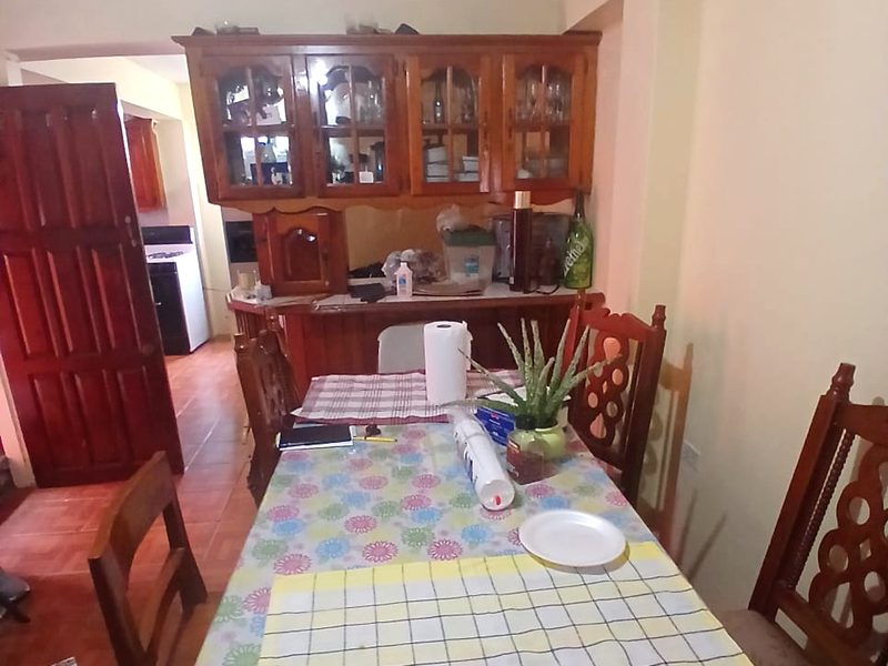 The dining area: a long table with carved wooden chairs, a wooden display cabinet behind it and the kitchen beyond