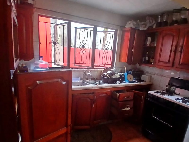 The kitchen sink area beneath a wide window with decorative security grilles, with wooden cabinets and a gas stove